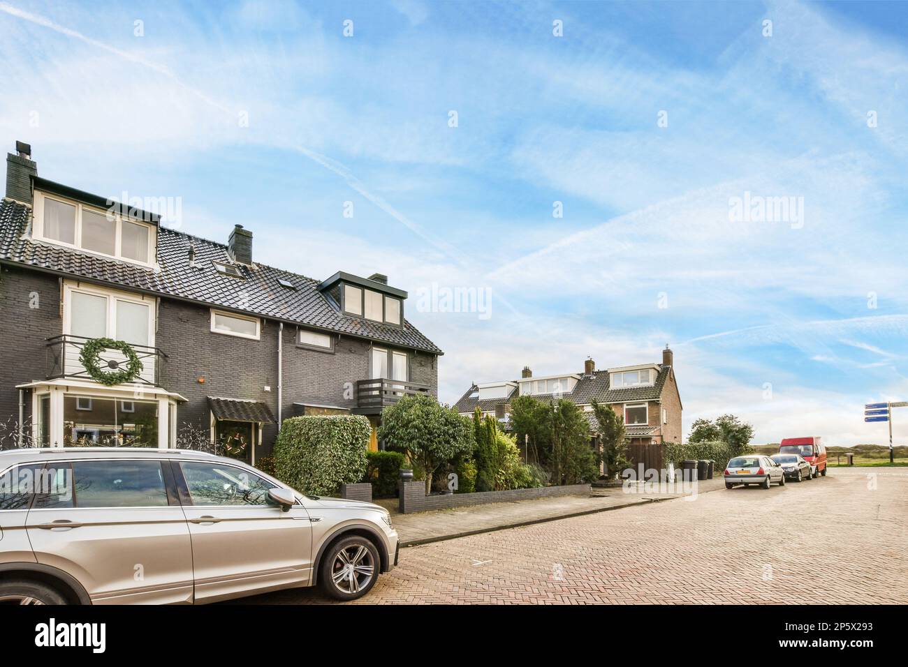 una macchina parcheggiata sul lato di una strada di fronte ad una casa con un cielo blu e nuvole bianche Foto Stock