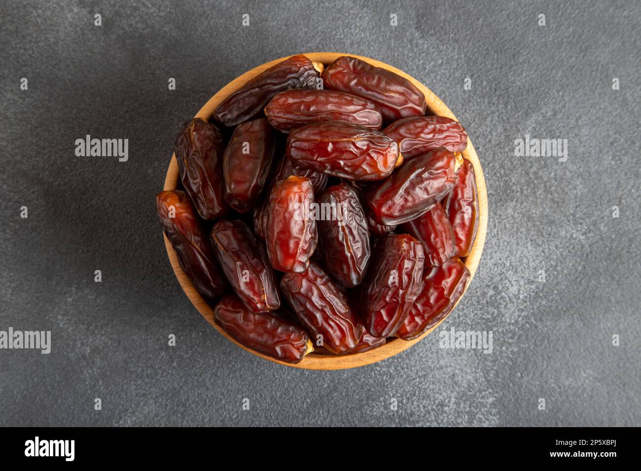 Frutta di data in ciotola di legno, su fondo nero Foto Stock