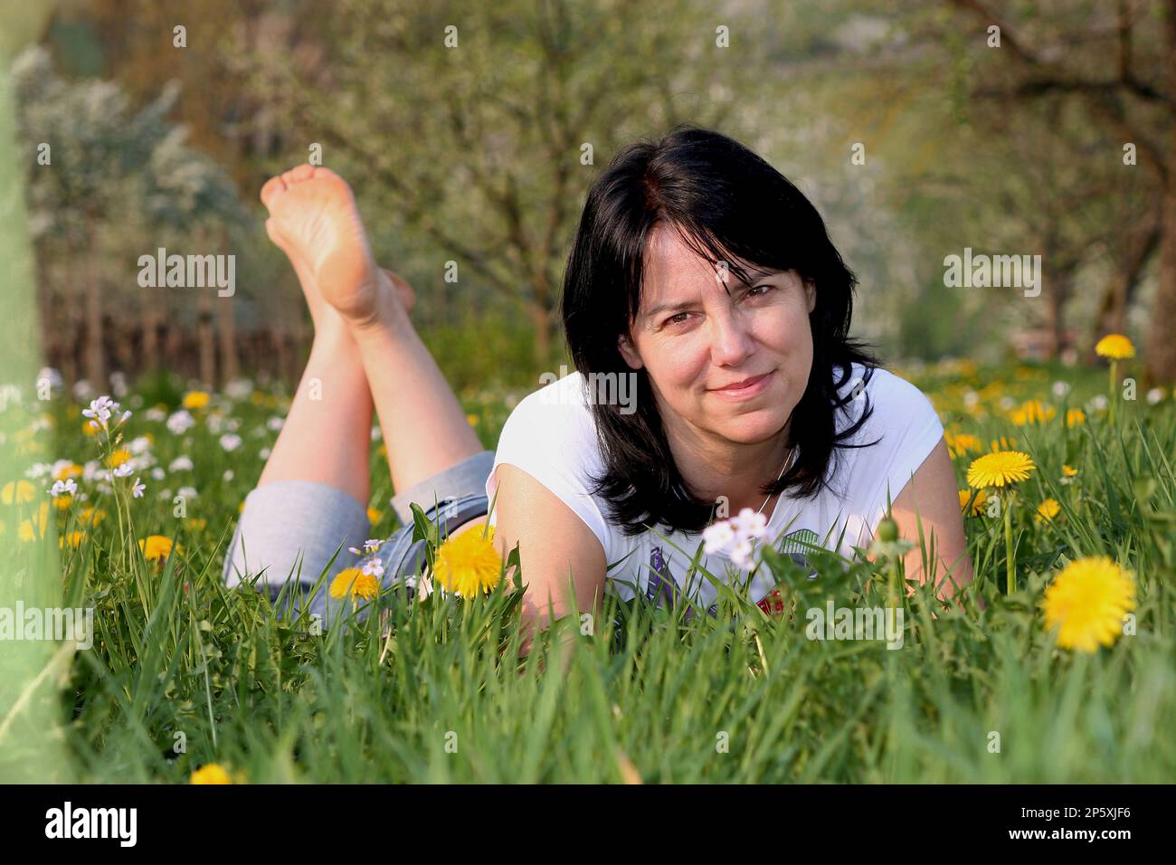 donna a piedi nudi si trova in un prato di dente di leone e rilassante Foto Stock