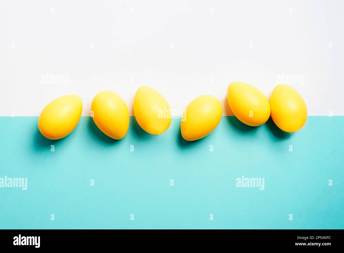 Uova di Pasqua gialle su sfondo bianco e blu. Vista dall'alto, disposizione piatta, spazio di copia. Foto Stock