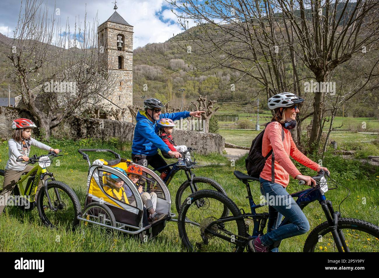 Famiglia in bicicletta e chiesa romanica di Sant Feliu, Barruera, Vall de Boí, Lleida, Catalogna, Spagna Foto Stock