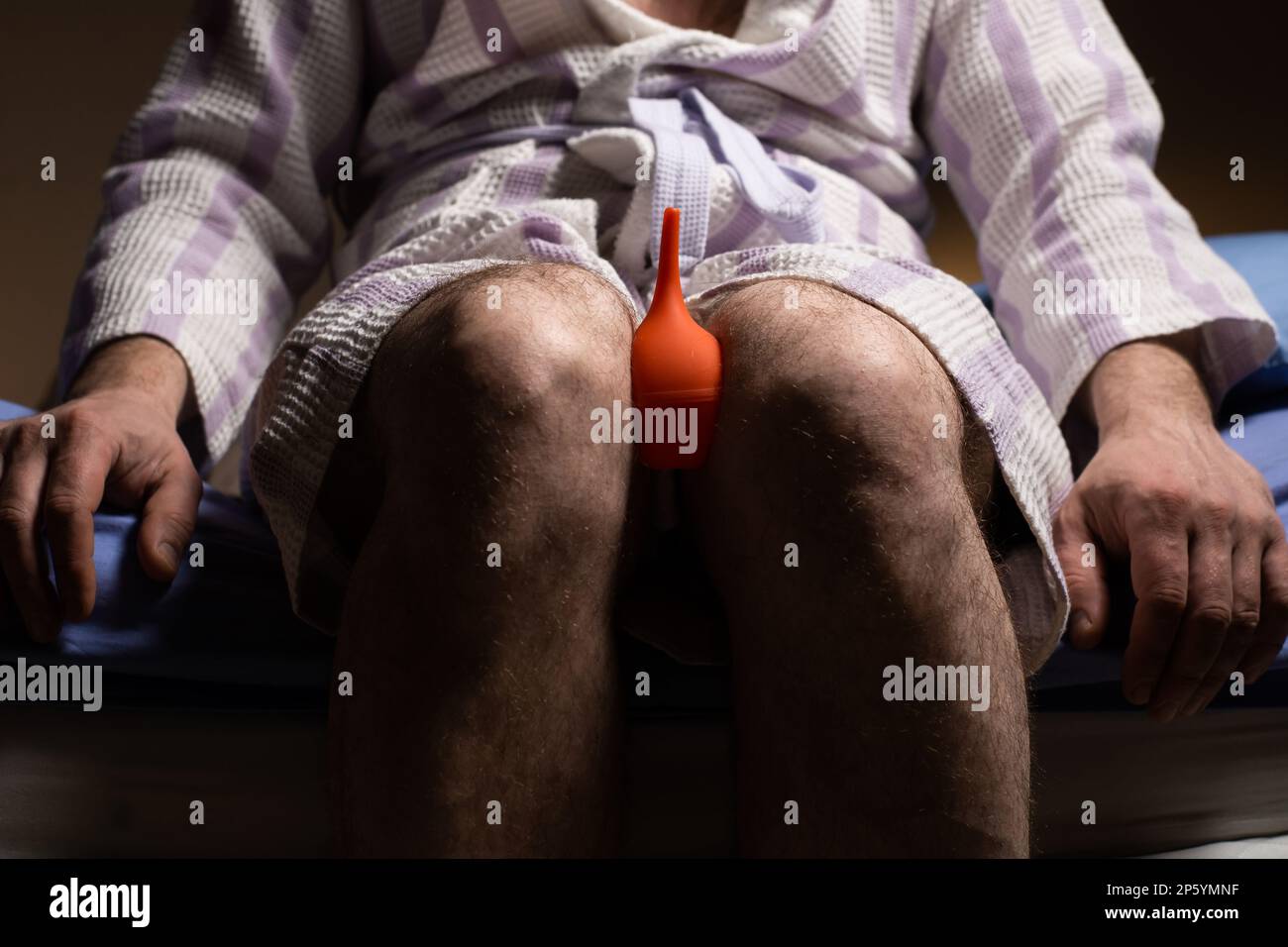 Concetto di costipazione. Un uomo irriconoscibile in un accappatoio tiene un clistere nelle sue mani. Disturbo del tratto digestivo. Foto Stock