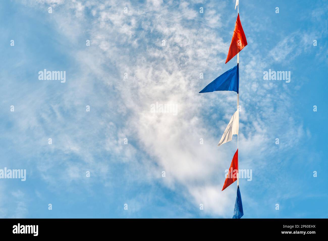 Garland di bandiere triangolari colorate pende sotto il cielo blu con nuvole di luce vista dal basso. Decorazione di festa per festa nella bella giornata di sole Foto Stock