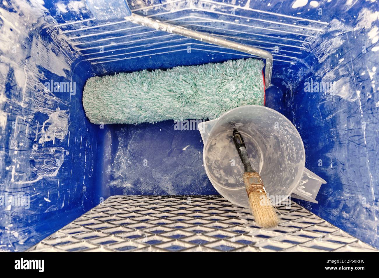 Secchio di plastica quadrato per pittura blu in piedi su cartone, sporco di vernice bianca asciutta, compresi gli strumenti di base come griglia, rullo, contenitore graduato, pennello Foto Stock