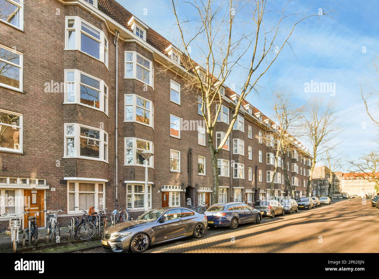 Amsterdam, Paesi Bassi - 10 aprile 2021: Alcune auto parcheggiate sul lato di una strada di fronte ad una fila di edifici in mattoni con finestre bianche Foto Stock
