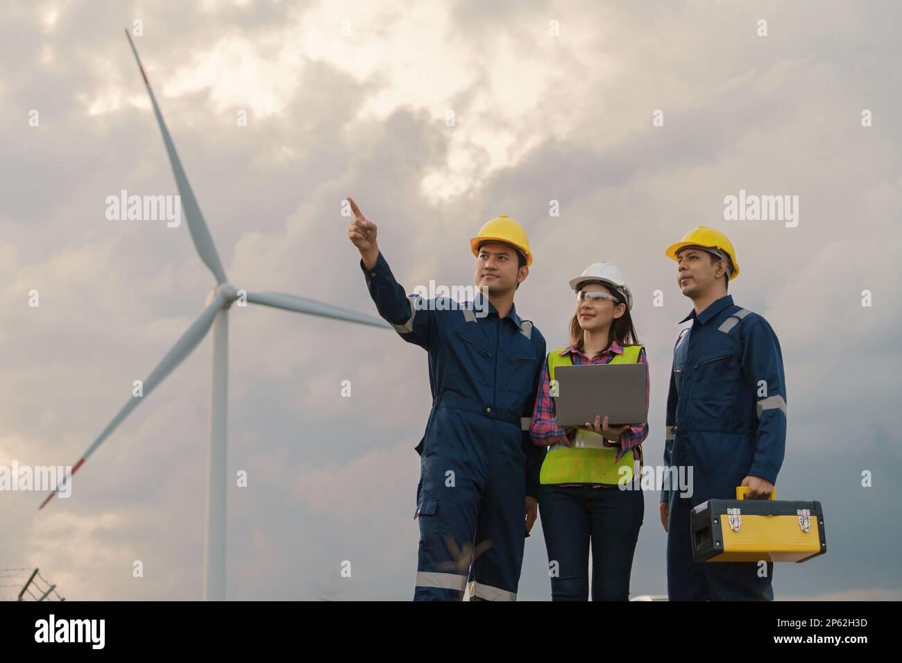 Tre tecnici tecnici in uniforme con la stazione di alimentazione della centrale di potenza della turbina eolica in piedi e di controllo. Energia pulita e ambiente. Foto Stock