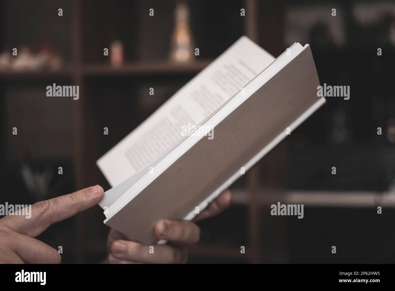 le mani degli uomini stanno tenendo un libro aperto in una copertina bianca su uno sfondo scuro. Foto Stock