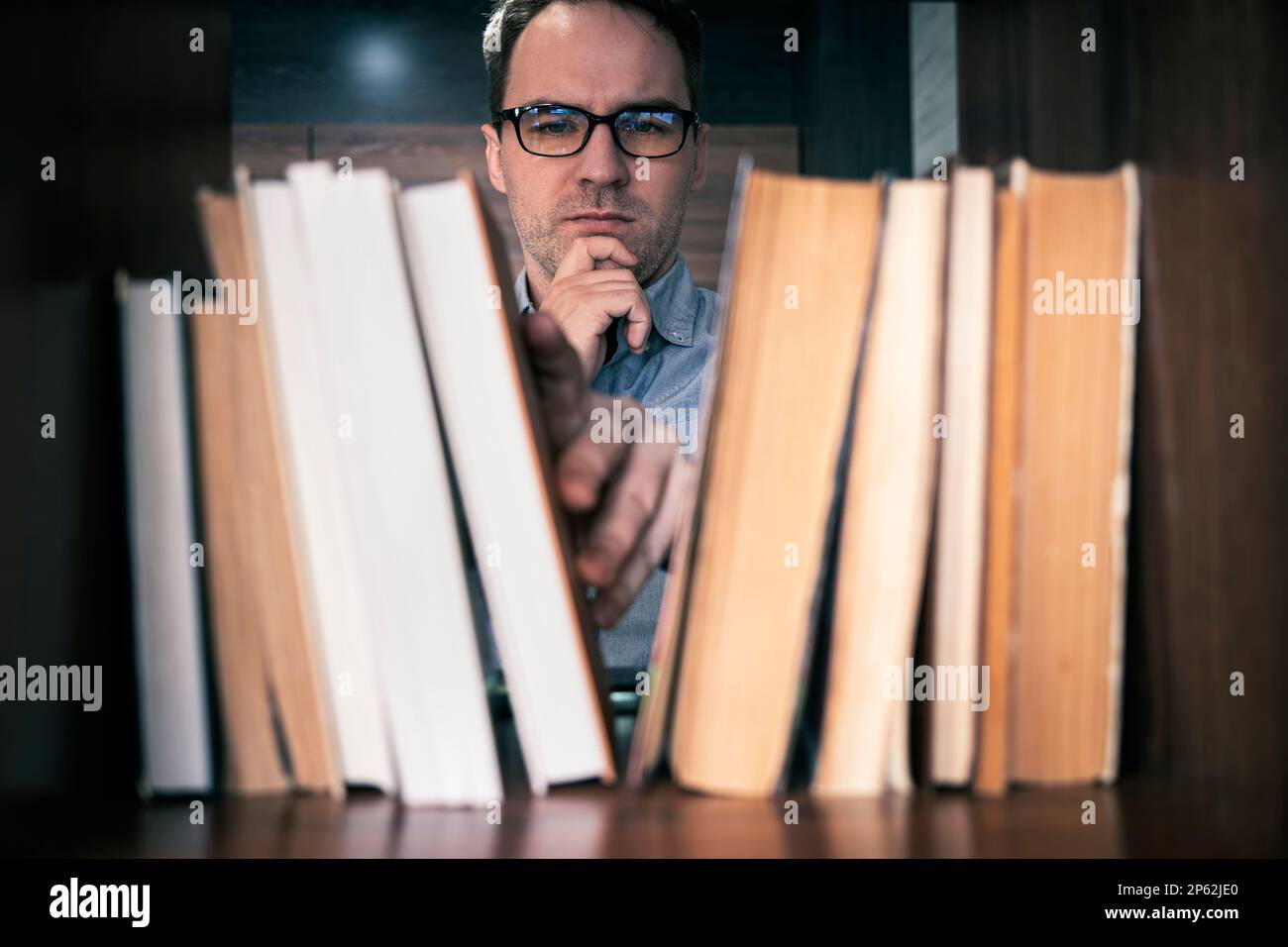 manuale maschile scelta e raccolta di libri in biblioteca pubblica, ricerca di istruzione e auto apprendimento in concetti di vita universitaria Foto Stock