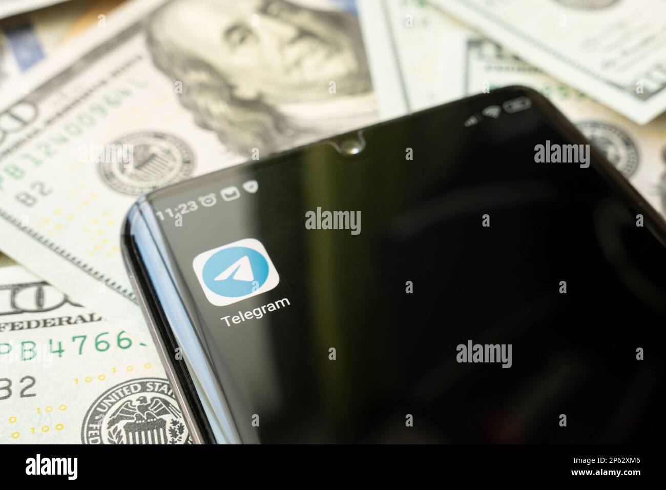 Schermo dello smartphone con l'app Telegram e molte banconote da cento dollari. Concetto di business e social networking. l'icona dell'applicazione sulla schermata nera Foto Stock