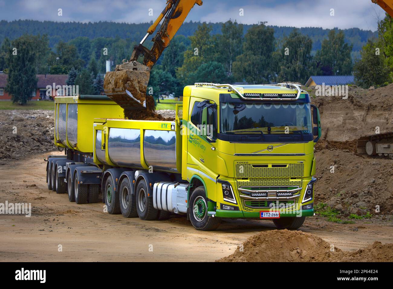 Escavatore cingolato che carica il terreno sul rimorchio a cassetta per autocarri Volvo FH16 verde. Salo, Finlandia. Agosto 27, 2022. Foto Stock