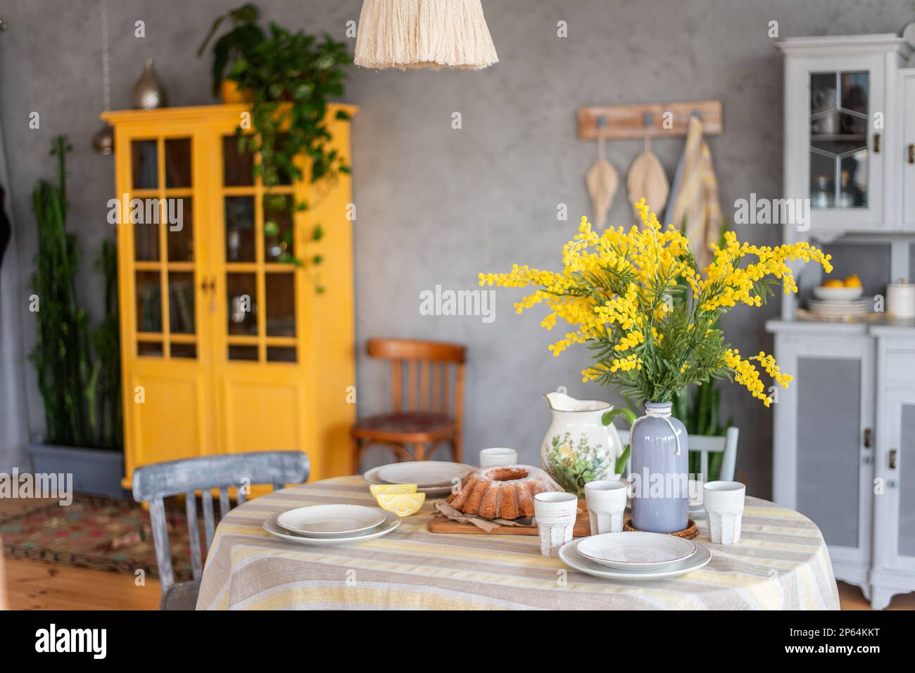 Primavera, Pasqua interni in stile scandinavo. Rustico soggiorno con un luminoso armadio, mimosa giallo in vaso. La tabella viene impostata in modo festivo con ceram Foto Stock