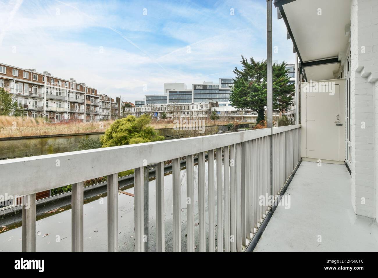 un balcone con alcuni edifici sullo sfondo e un fiume che lo attraversa, visto dalla finestra di un appartamento Foto Stock