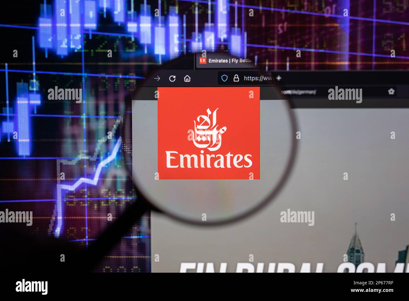 Emirates compagnia aerea logo su un sito web con blurry mercato azionario sviluppi in background, visto su uno schermo attraverso una lente di ingrandimento Foto Stock