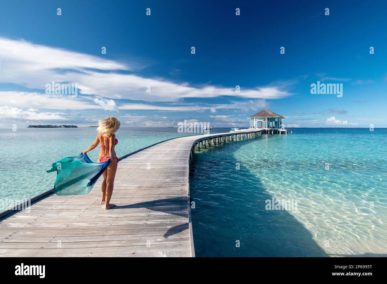 Giovane donna con un sarong a piedi sul molo di legno di un resort maldiviano Foto Stock