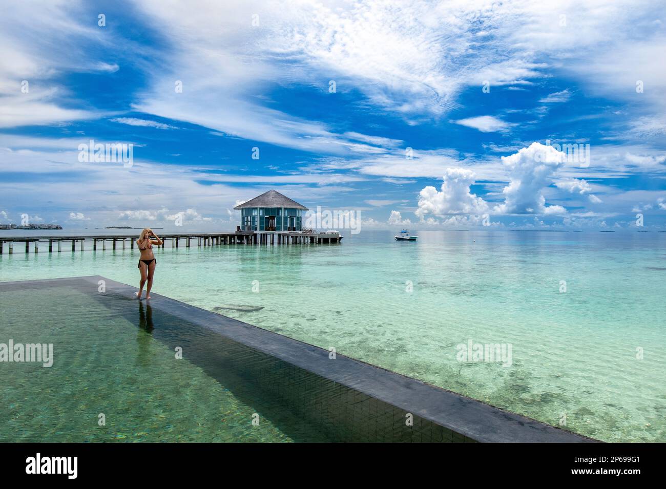 Giovane donna che cammina lungo il bordo di una piscina infinity, Maldive Foto Stock