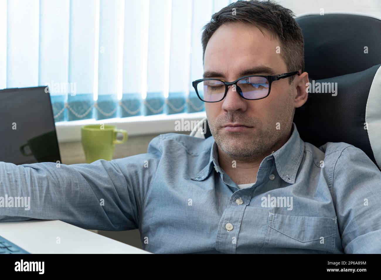 Giovane uomo d'affari in camicia blu che dorme sulla scrivania in ufficio Foto Stock