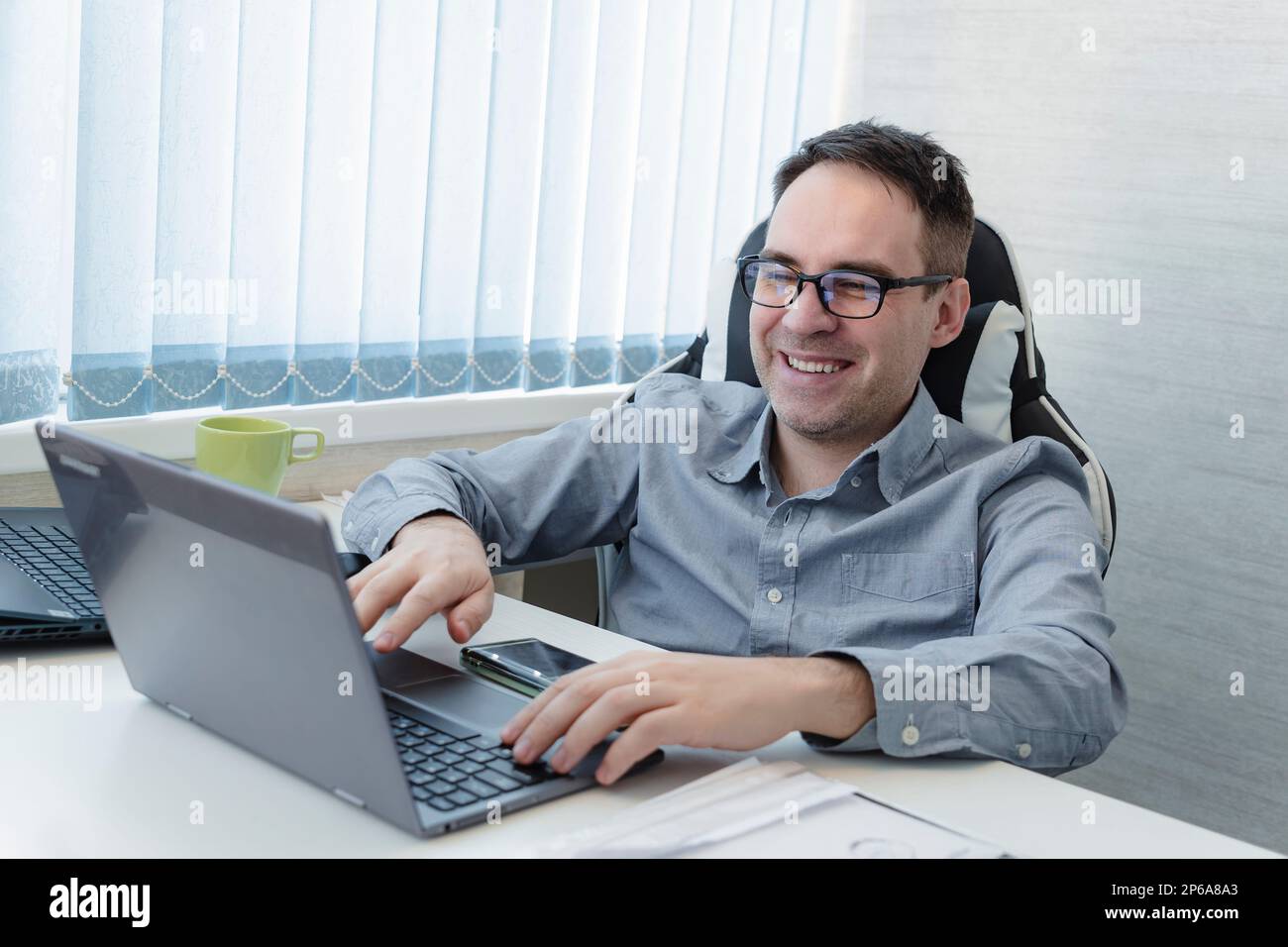 Giovane uomo sorridente che lavora su un computer portatile in cucina moderna, controllare la posta elettronica al mattino, scrivere un messaggio in rete sociale, uomo felice utilizzando internet, ricerca Foto Stock