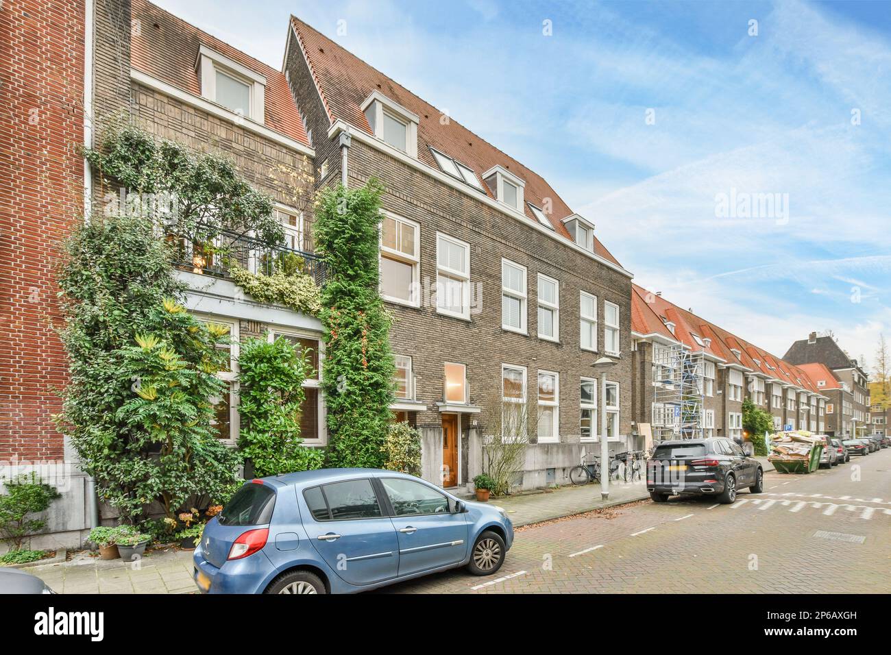 Amsterdam, Paesi Bassi - 10 aprile, 2021: Una strada cittadina con auto parcheggiate sui marciapiedi e gli edifici in mattoni in lontananza è un cielo blu che ha alcune nuvole bianche Foto Stock