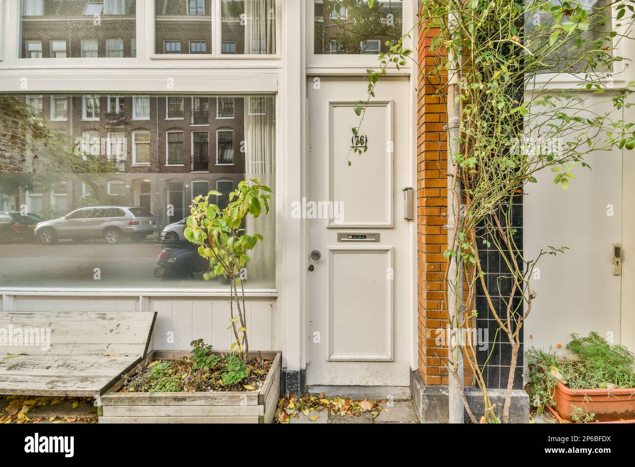 Amsterdam, Paesi Bassi - 10 aprile, 2021: Alcune piante di fronte ad una casa con una macchina parcheggiata accanto alla porta e dietro di essa è un edificio in mattoni Foto Stock