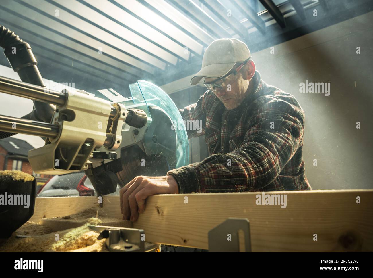 L'appaltatore caucasico Carpenter Woodwork Technician nel suo 40s tagliando a misura pezzi di travi di legno usando potente sega di legno. Foto Stock