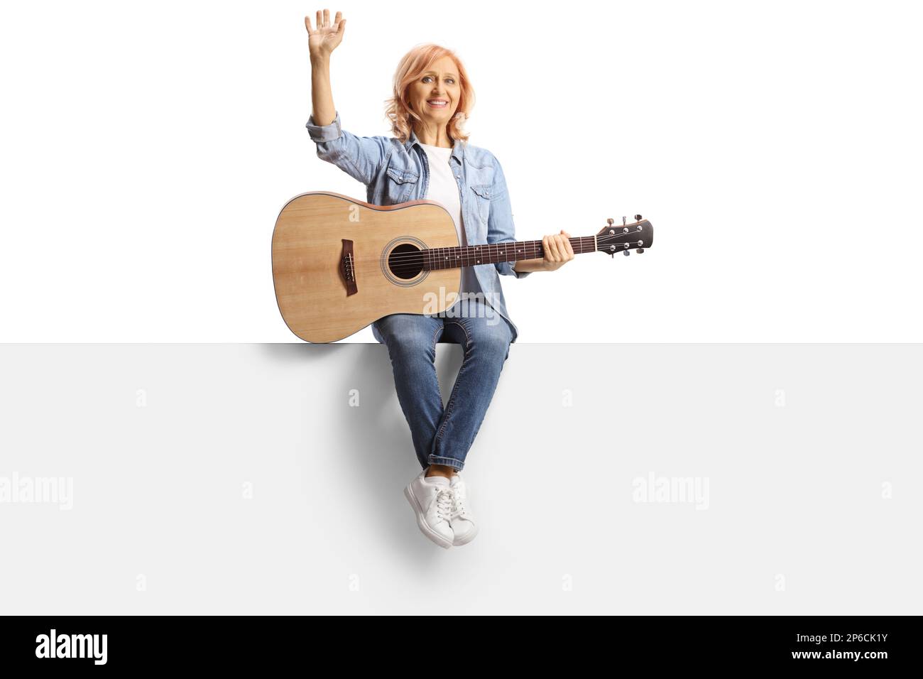 Ritratto a tutta lunghezza di una donna seduta su un pannello con una chitarra acustica e isolata ondeggiante su sfondo bianco Foto Stock