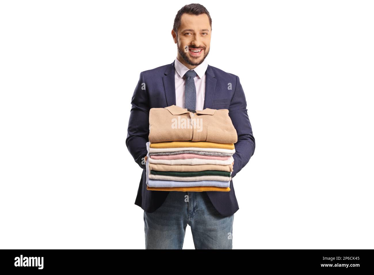 Giovane uomo che tiene un mucchio di vestiti piegati e sorridente alla macchina fotografica isolata su uno sfondo bianco Foto Stock