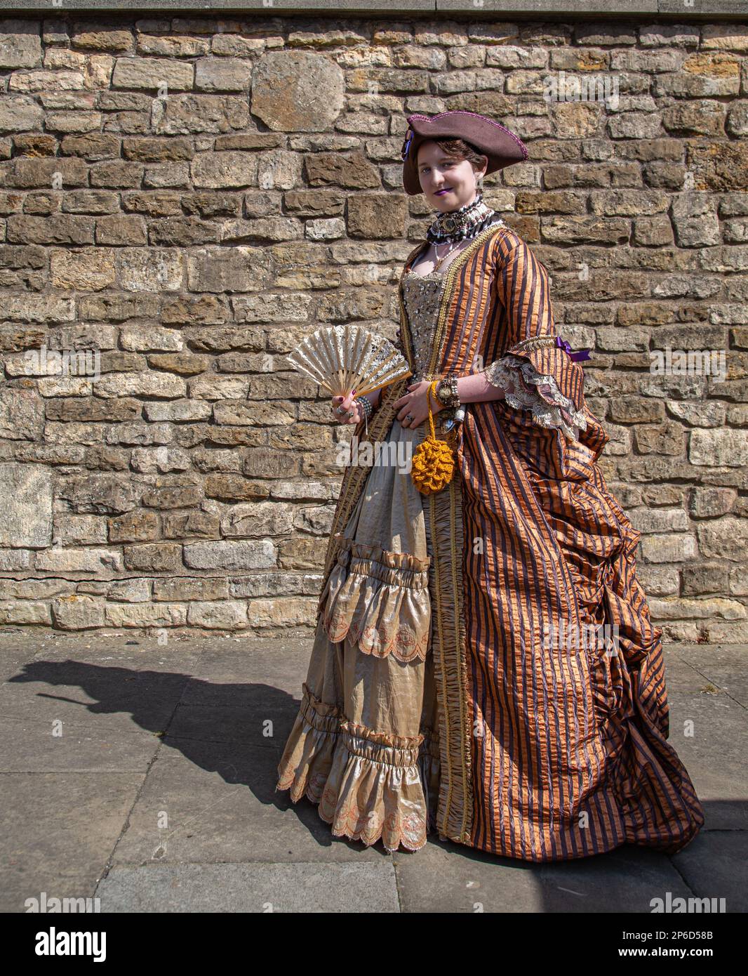 Una donna che indossa un vestito d'epoca con un ventilatore e sorridente direttamente alla macchina fotografica. Foto Stock