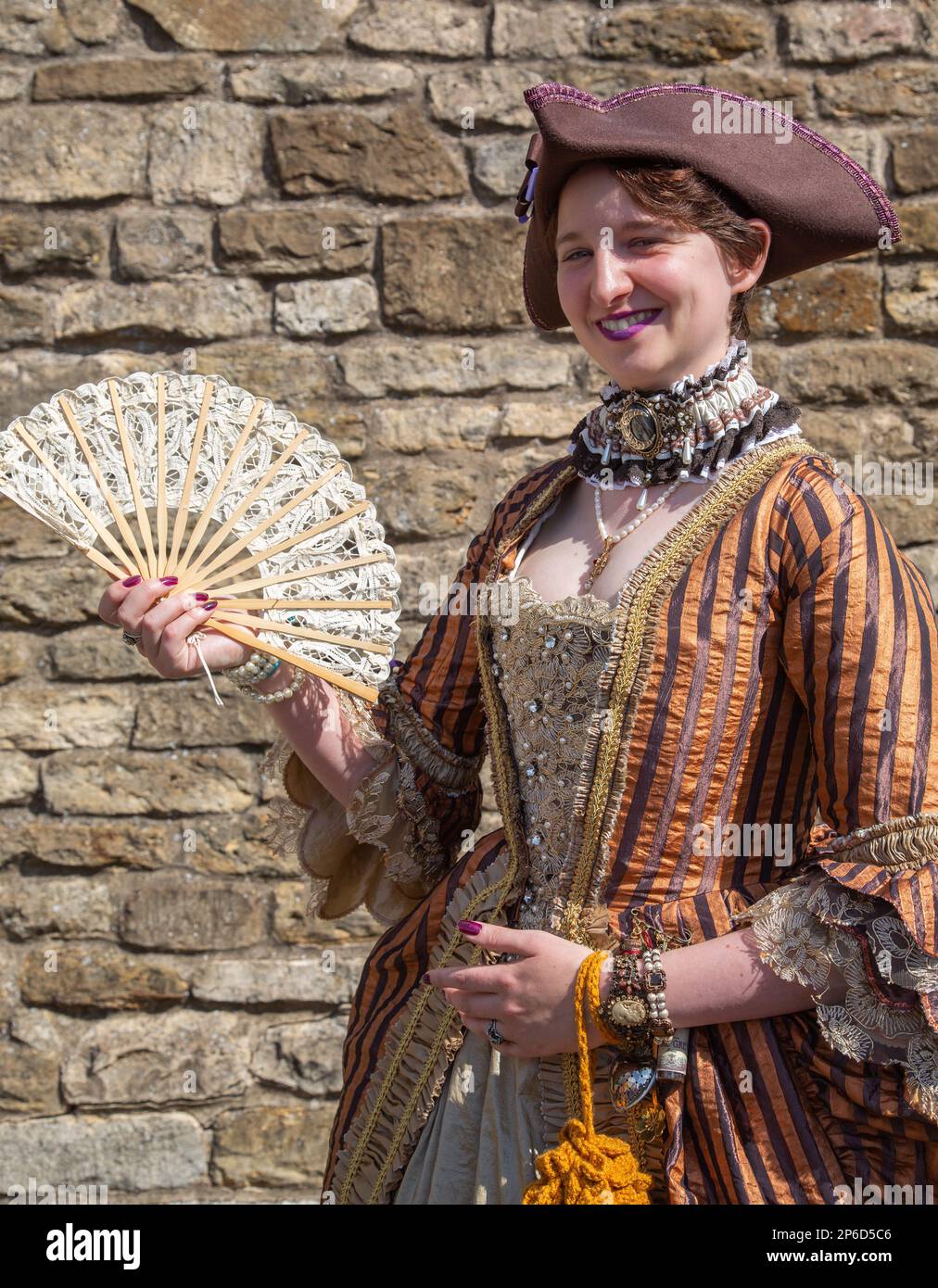 Una donna che indossa un vestito d'epoca con un ventilatore e sorridente direttamente alla macchina fotografica. Foto Stock
