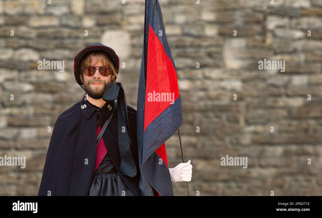 Un uomo con una barba, vestito in una divisa femminile dell'Esercito della salvezza, che tiene una bandiera e guarda direttamente nella fotocamera. Spazio di copia. Foto Stock