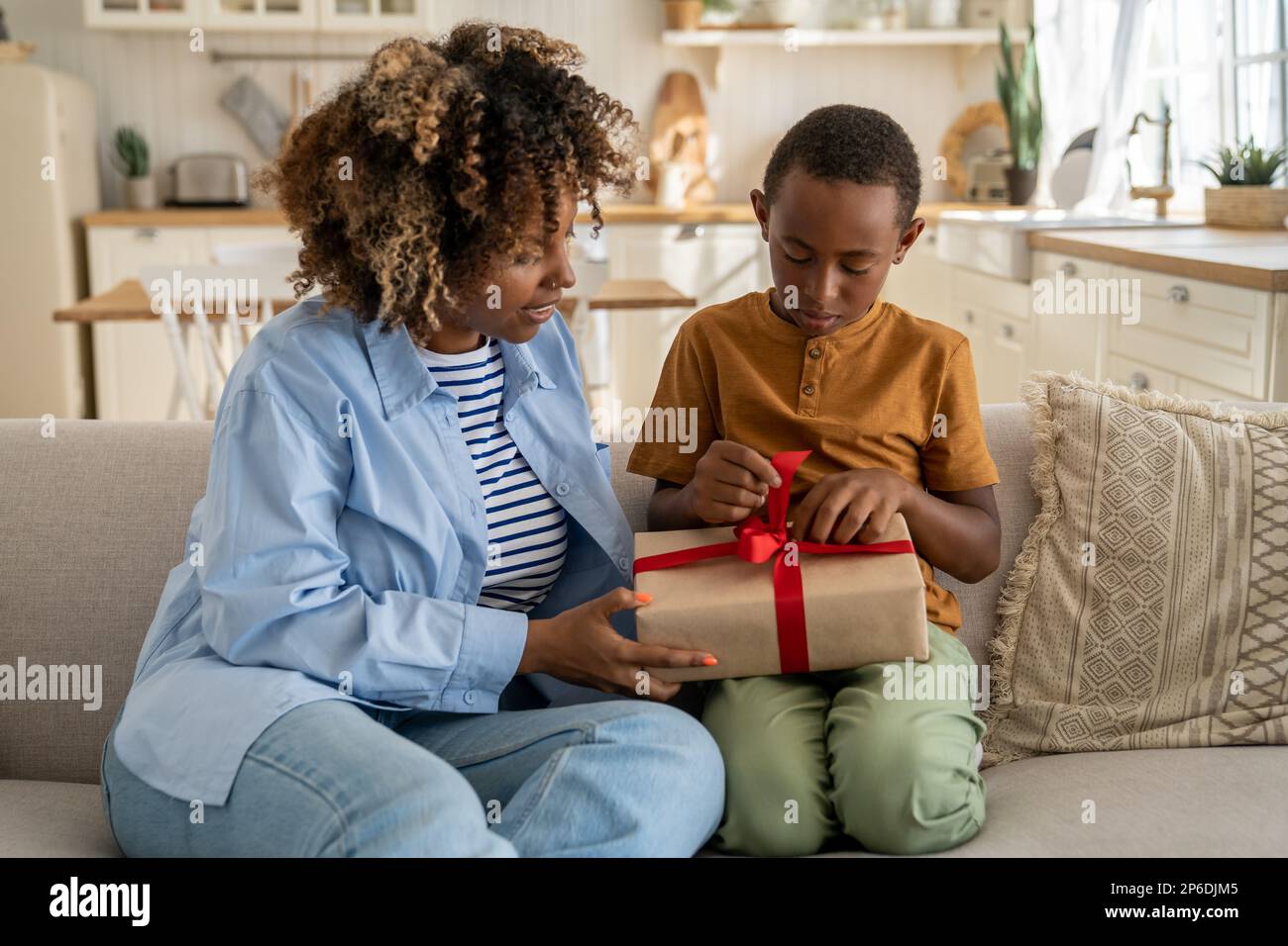 Amorevole donna nera mamma si congratula felice piccolo figlio con compleanno dare regalo avvolto con nastro rosso Foto Stock