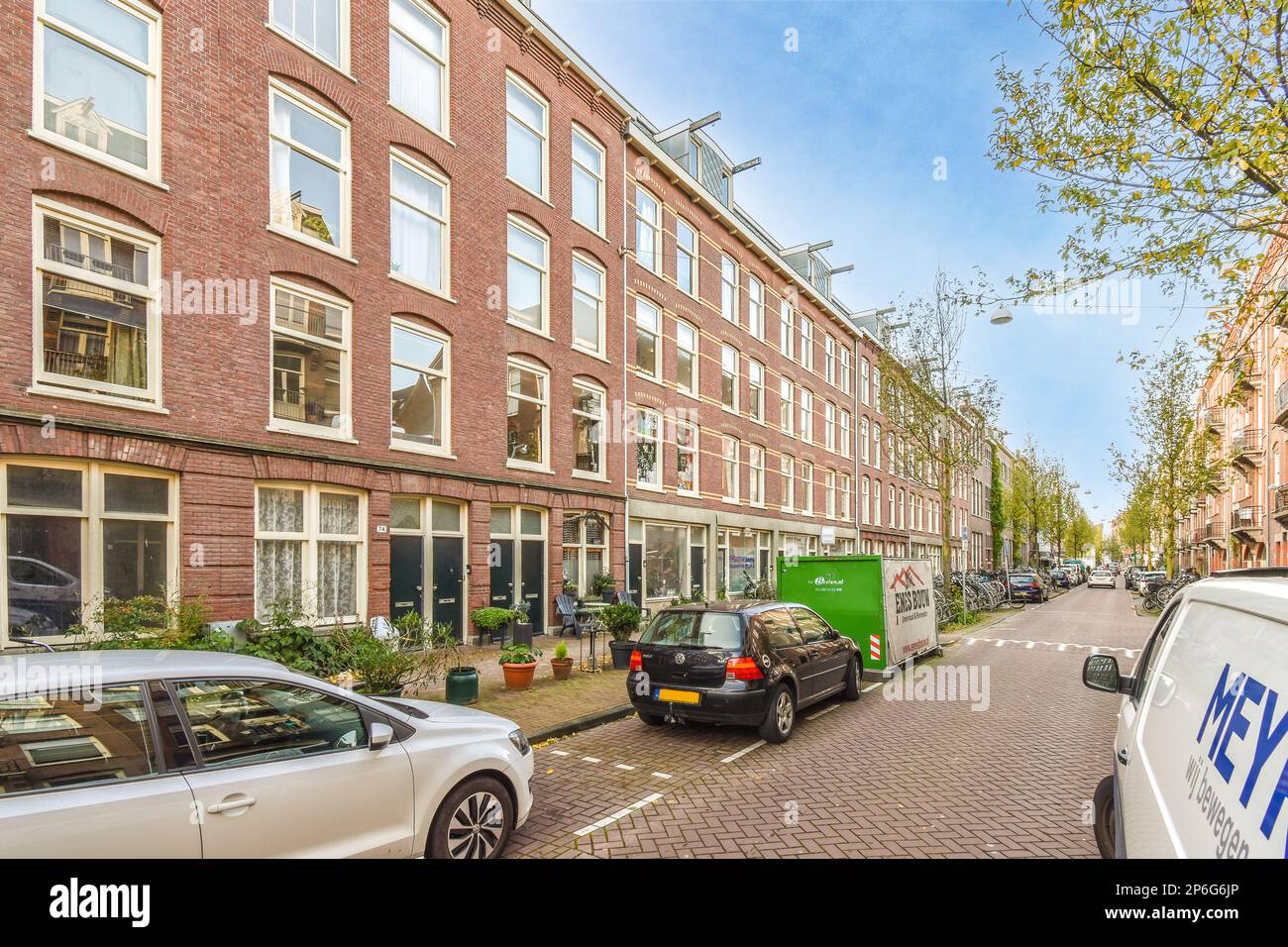 Amsterdam, Paesi Bassi - 10 aprile 2021: Una strada cittadina con auto parcheggiate lateralmente e edifici sullo sfondo, compreso un furgone bianco che percorre la strada Foto Stock