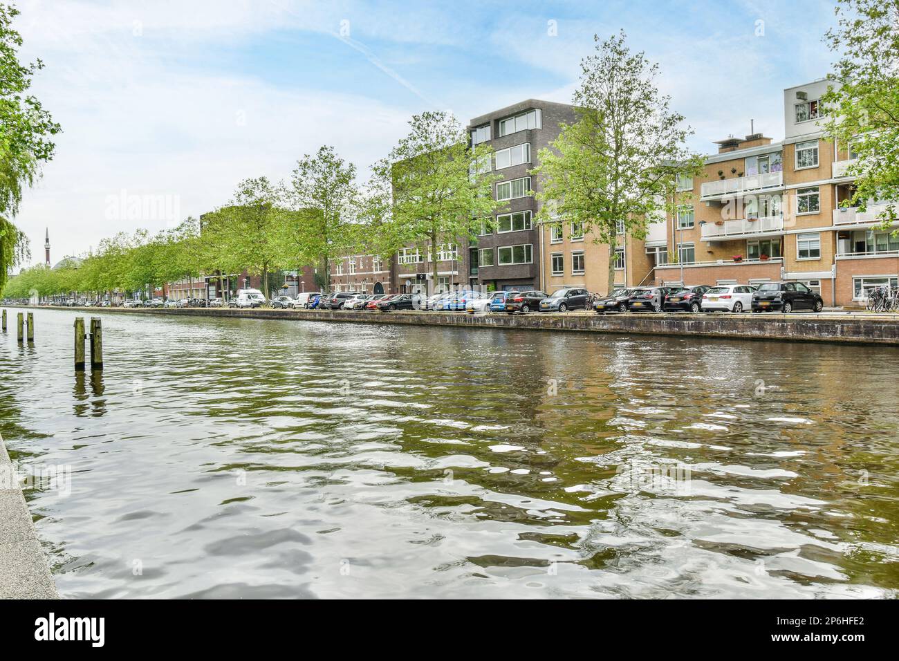 Amsterdam, Paesi Bassi - 10 aprile, 2021: Alcuni edifici sul lato di un corpo d'acqua con auto parcheggiate lungo di esso e alberi nelle fortune Foto Stock