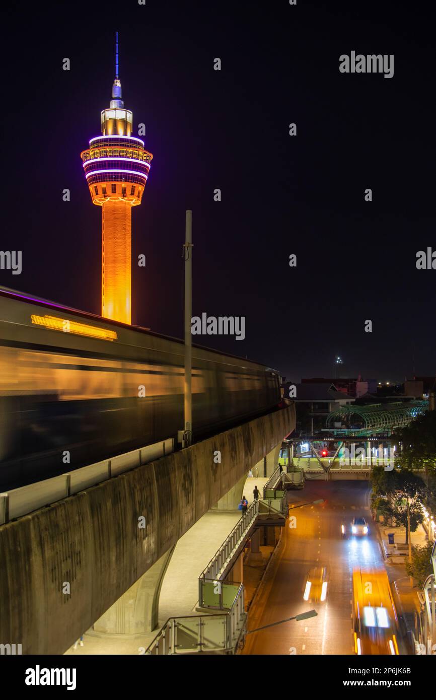 SAMUT PRAKAN, THAILANDIA, DEC 03 2022, il treno notturno viaggia sul viadotto sotto la torre di osservazione illuminata Foto Stock