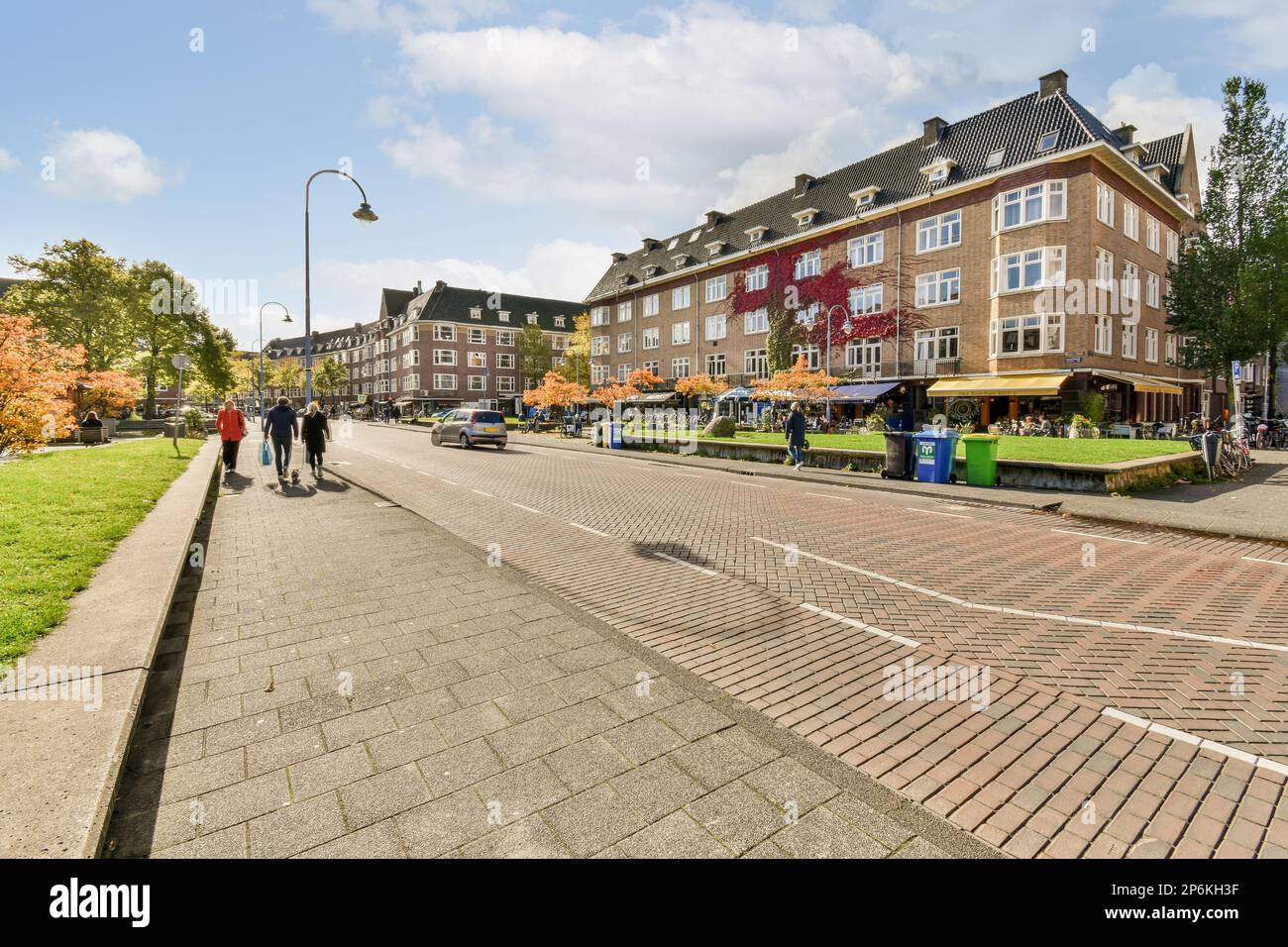 Amsterdam, Paesi Bassi - 10 aprile, 2021: Persone che camminano lungo la strada di fronte ad alcuni edifici in una giornata di sole con cielo blu e nuvole bianche e soffici Foto Stock