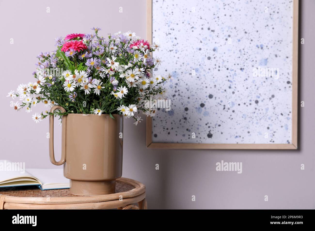 Elegante vaso in ceramica con splendidi fiori e libro aperto sul tavolo in  vimini vicino a una parete chiara Foto stock - Alamy