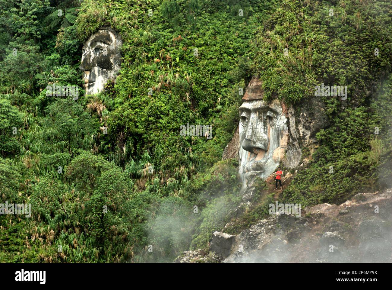 Un visitatore è avvistato vicino a una formazione gigante del volto che illustra il carattere di Toar, che, insieme a Lumimuut (visto in lontananza) Sono creduti come gli antenati del popolo di Minahasan secondo la mitologia locale, a Bukit Kasih, una destinazione popolare per il turismo culturale, naturale e religioso situato nel villaggio di Kanonang, Kawangkoan occidentale, Minahasa, Sulawesi settentrionale, Indonesia. Foto Stock