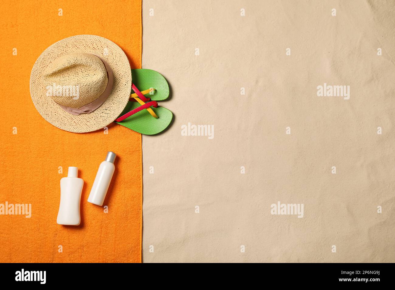 Telo da spiaggia, cappello, prodotti per la protezione solare e infradito sulla sabbia, giacitura piatta. Spazio per il testo Foto Stock