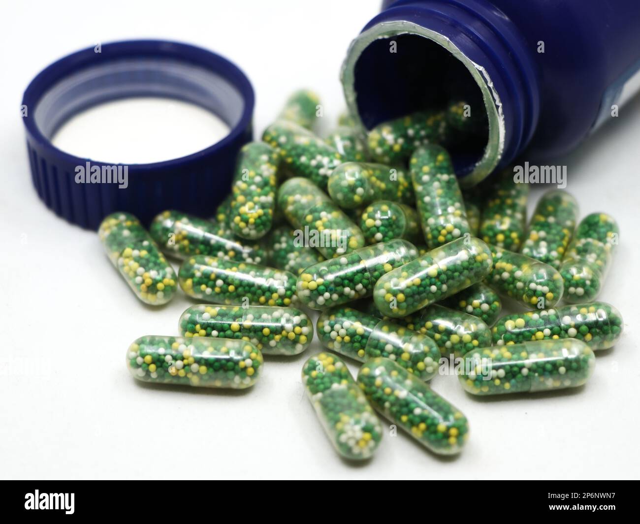 capsule con pillole verdi, gialle e bianche contenenti integratori vitaminici e nutrienti sparsi da una bottiglia blu isolata su sfondo bianco Foto Stock