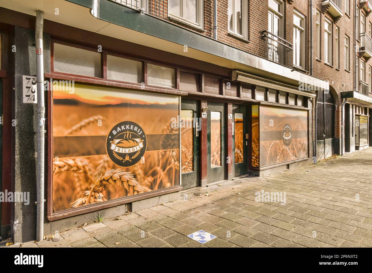 Amsterdam, Paesi Bassi - 10 Aprile, 2021: Un annuncio sul lato di un edificio di fronte ad un edificio in mattoni con due finestre e una porta aperta Foto Stock