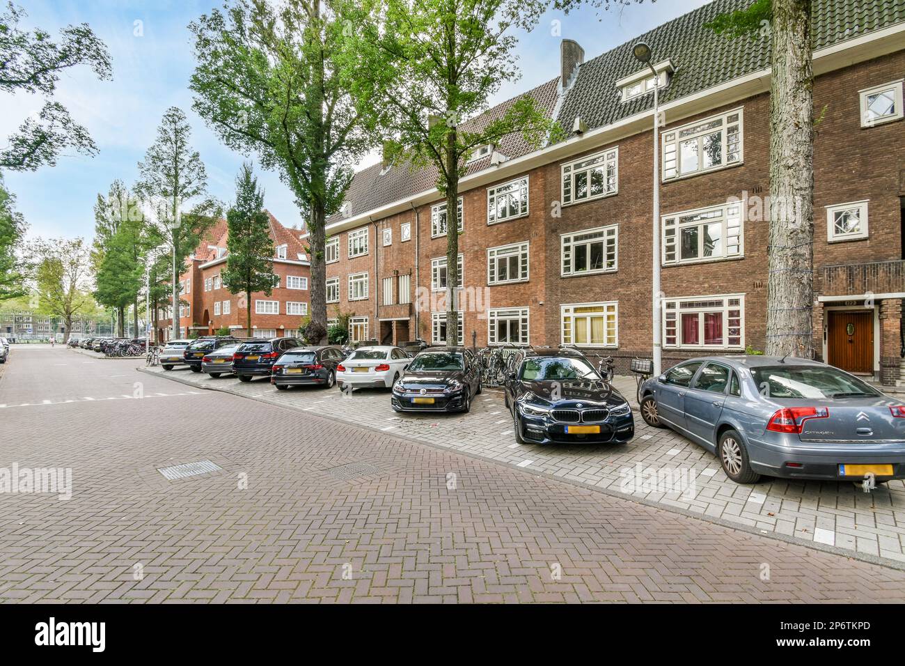 Amsterdam, Paesi Bassi - 10 aprile 2021: Alcune auto parcheggiate sul lato di una strada di fronte a una fila di edifici in mattoni rossi con finestre bianche Foto Stock