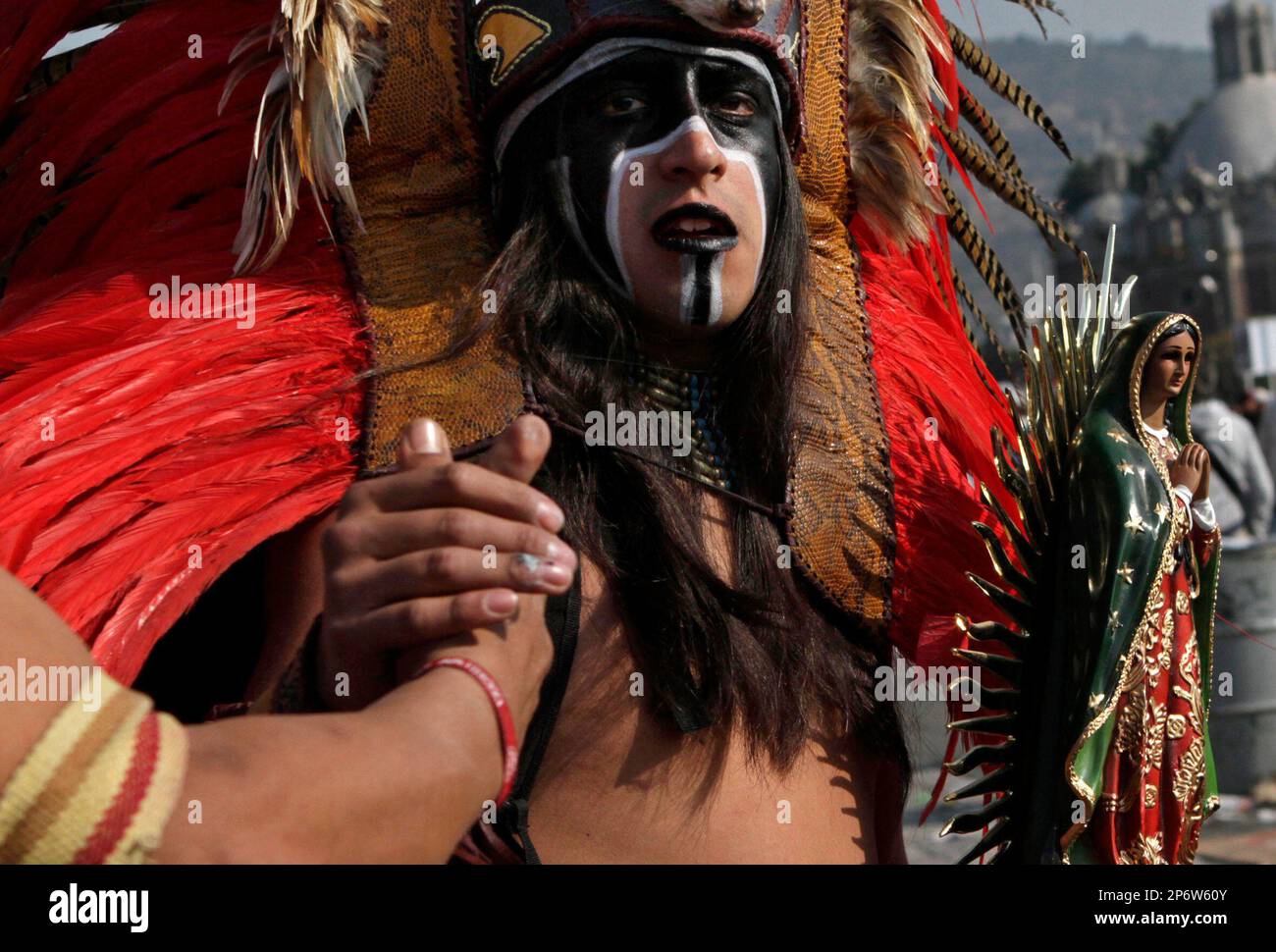 Aztec dancer Ehecatonatihu greets a friend while carrying a statue of ...