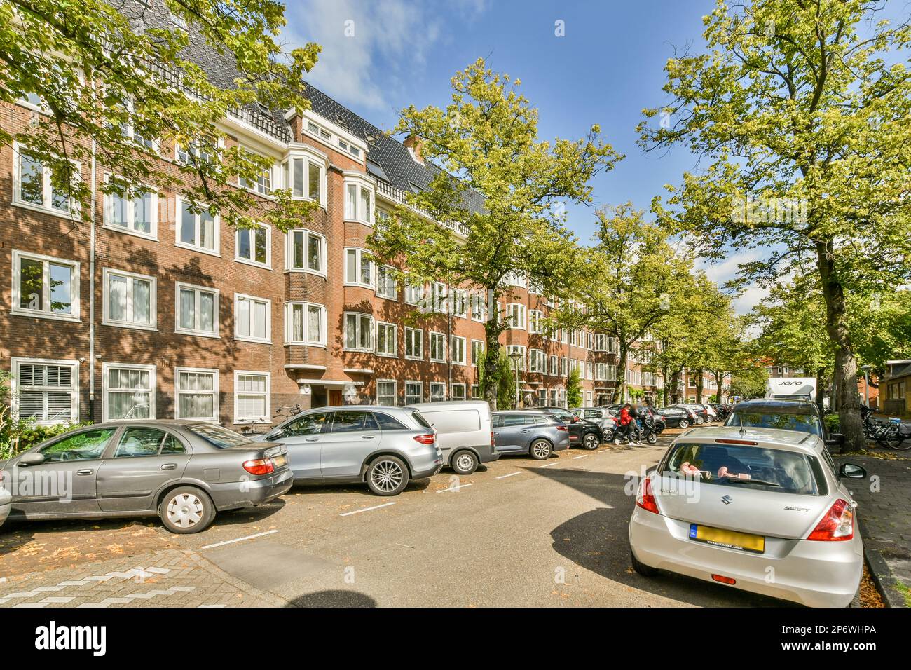 Amsterdam, Paesi Bassi - 10 aprile 2021: Alcune auto parcheggiate sul lato della strada di fronte ad una fila di edifici in mattoni con finestre bianche Foto Stock