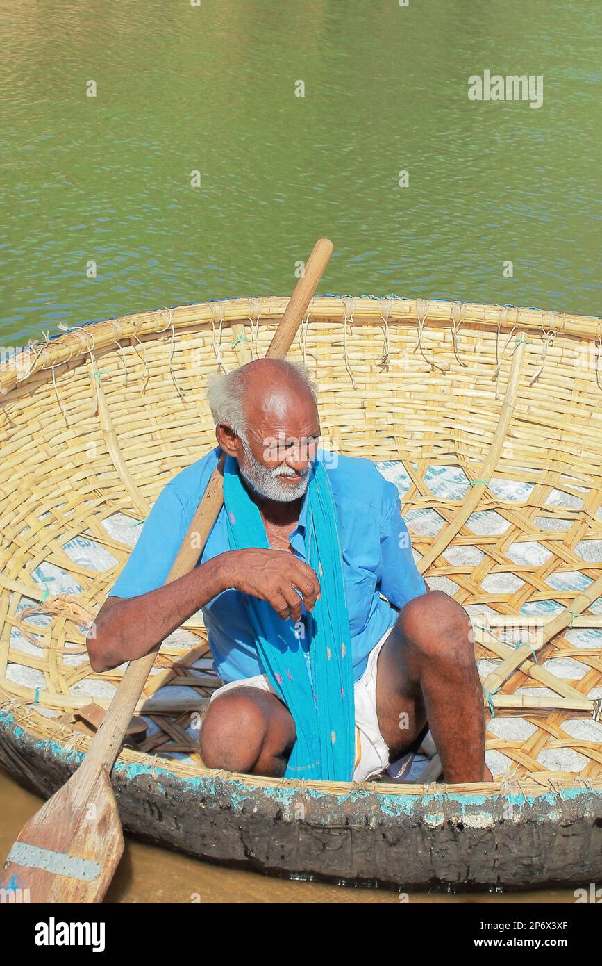 Hogenakkal, Tamilnadu, India - 5th dicembre 2018: Vecchio barcaiolo e il suo coraclo sulla riva del fiume kaveri Foto Stock