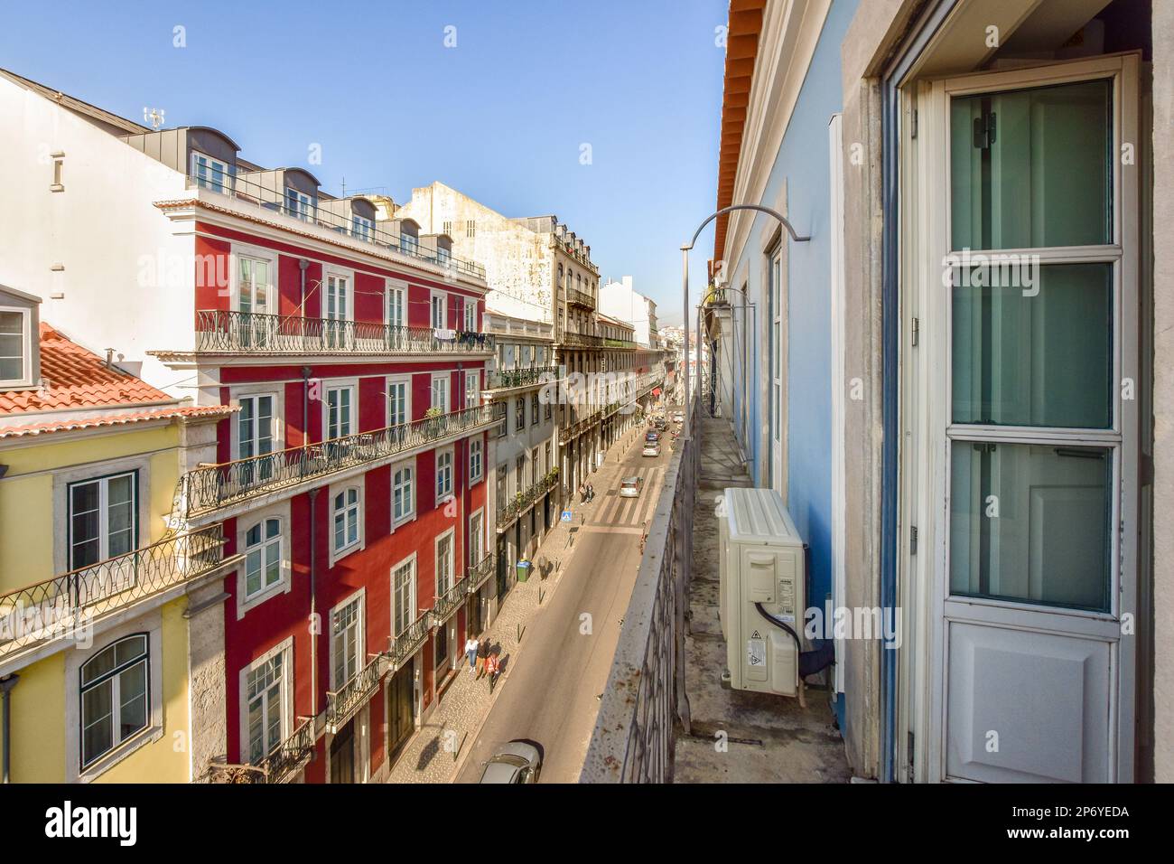 una strada urbana con edifici sullo sfondo e persone che camminano sul marciapiede, come si vede da una finestra del balcone Foto Stock