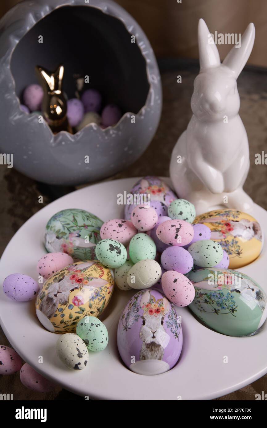 foto un sacco di grandi e piccole uova decorative luminose giacenti su un piatto bianco e accanto ad esso è un coniglio bianco su un tavolo di vetro Foto Stock