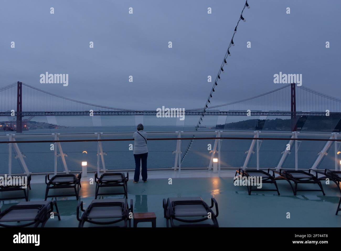 Ponte 25 de Abril a Lisbona/Ponte sul fiume Tagus - una sola donna passeggero su una nave da crociera al mattino presto guarda come ci si avvicina al ponte. Foto Stock