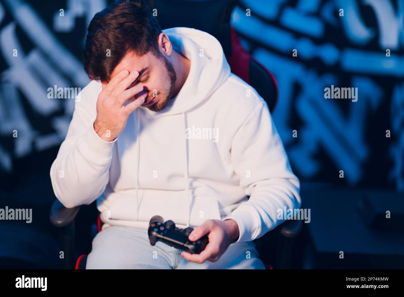 Giovane uomo noob newbie giocatore perdita giocare sulla console di gioco con gamepad seduto sulla sedia. Foto Stock