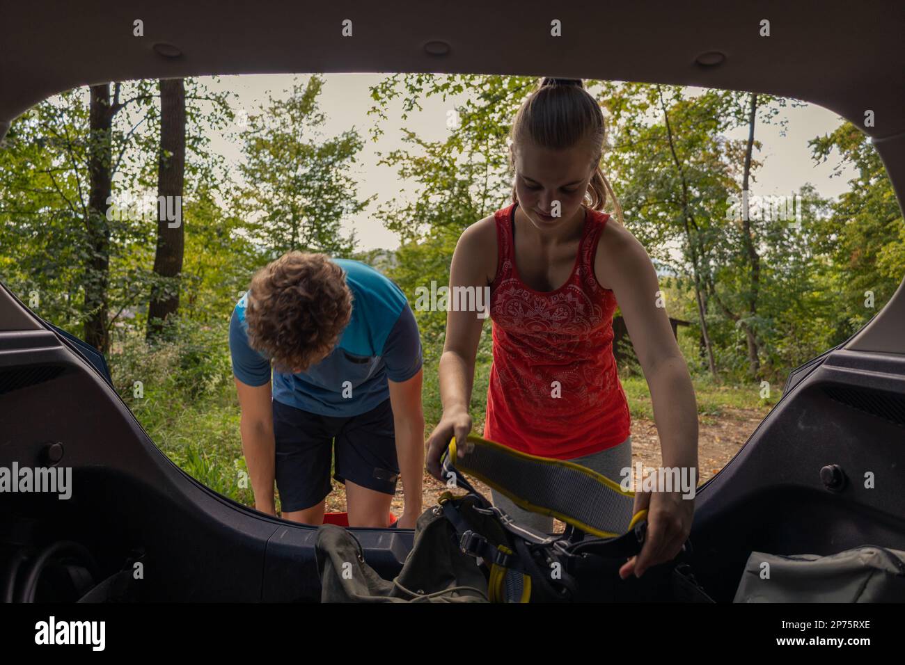 Giovane arrampicatore maschio e femmina che prende l'attrezzatura di arrampicata dal bagagliaio dell'auto e mette le imbracature sopra. Foto Stock