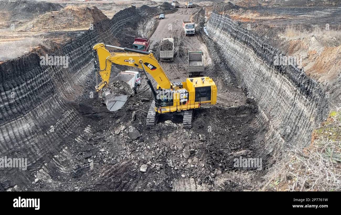 Escavatore che lavora su un enorme cantiere minerario, che carica i camion, che trasportano il materiale. Foto Stock