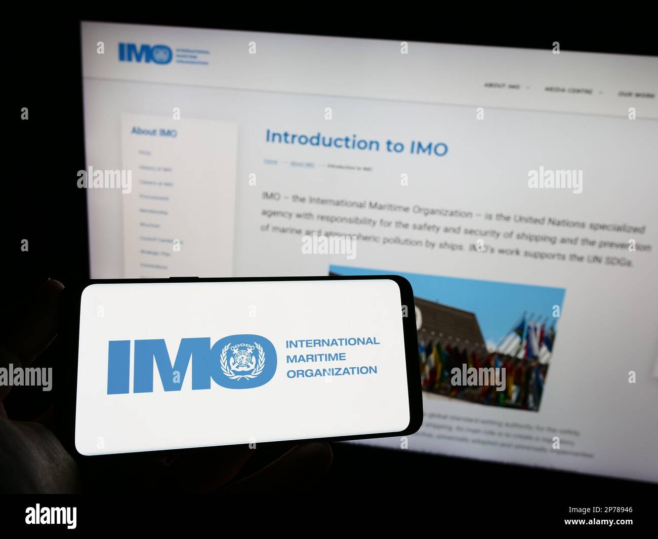 Persona che tiene un telefono cellulare con il logo dell'Organizzazione marittima internazionale (IMO) sullo schermo davanti alla pagina Web. Messa a fuoco sul display del telefono. Foto Stock